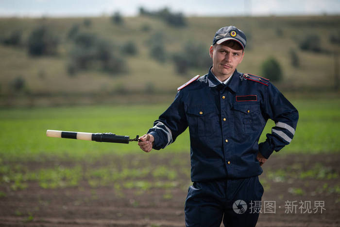 美丽的年轻警察身着军装, 手里拿着一根棍子在乡村风景的背景下