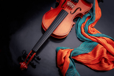 一张黑色桌子上的小提琴, 上面有一条彩色的橙色蓝色围巾。