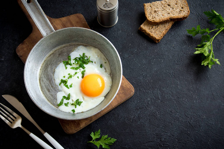 煎蛋在煎锅里吃早饭。煎蛋用面包和欧芹在煎锅之上黑石桌, 上部看法, 拷贝空间