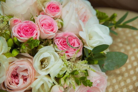 白金结婚戒指。新娘和新郎的两个白金戒指和一束粉红色的玫瑰和白色的花朵