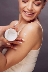 妇女应用美容护肤霜的保护和保健。一个年轻的微笑的女人拿着奶油。皮肤特写概念
