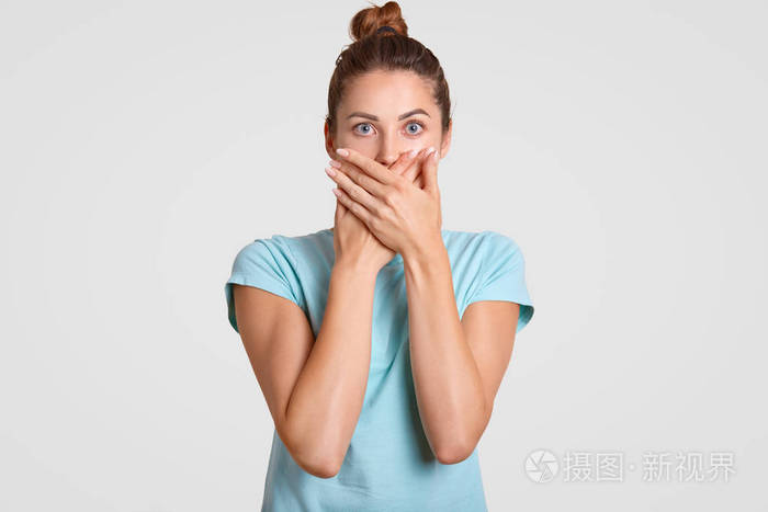 受惊的女人用两只手掌遮住嘴巴, 直视镜头看着惊恐的