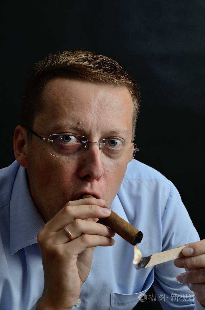 男模特35岁戴眼镜的男士, 身穿淡蓝色衬衣, 点燃雪茄