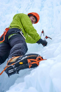 登山人用冰工具斧头在橙色的头盔上爬上一大块冰墙。户外运动 Portrai