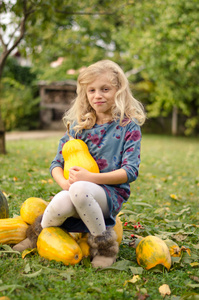 美丽的金发女孩与绿色秋花园里的橙色南瓜