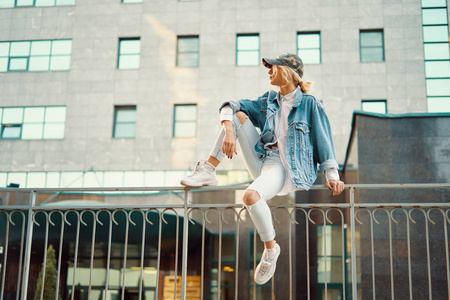 漂亮的女孩坐在一个欧洲城市的围栏栏杆上, 在后台的现代建筑, 同时