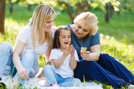 孩子吃冰淇淋与她的祖母和妈妈一起坐在绿色公园里