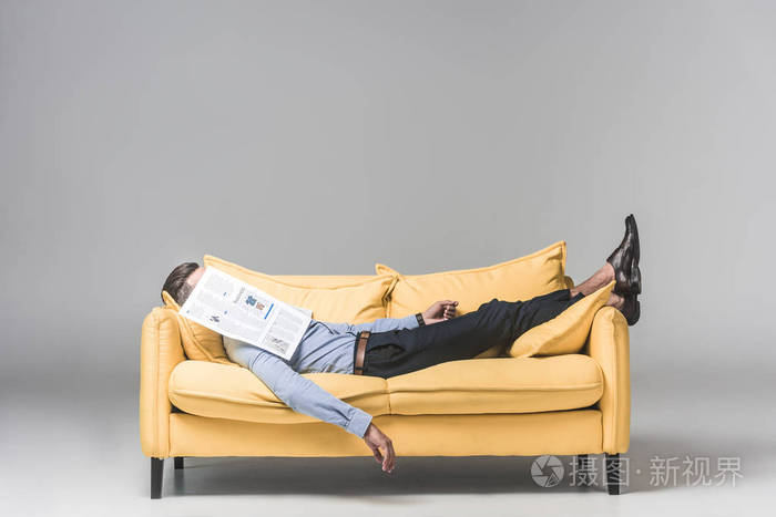 疲惫的商人睡在黄色的沙发上, 脸上的报纸, 灰色