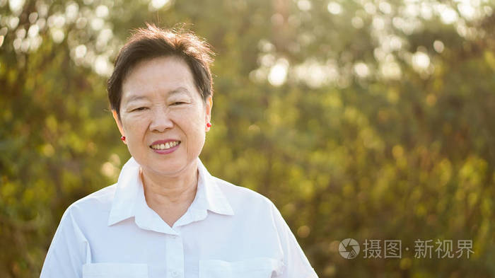 快乐亚洲老年妇女微笑在早晨阳光与绿色自然背景