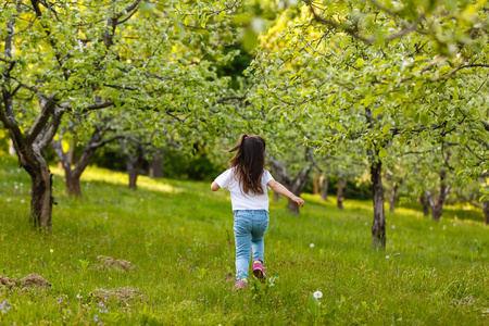 美丽的小女孩奔跑在绿色春天庭院里照片