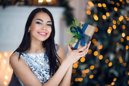 美丽的年轻妇女与礼品盒附近的圣诞树上的颜色背景