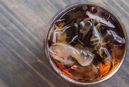 可乐饮料在玻璃上与冰在木桌顶部