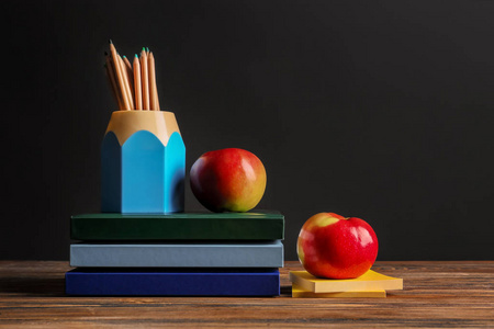 一套学校文具与苹果在木桌反对黑暗的背景