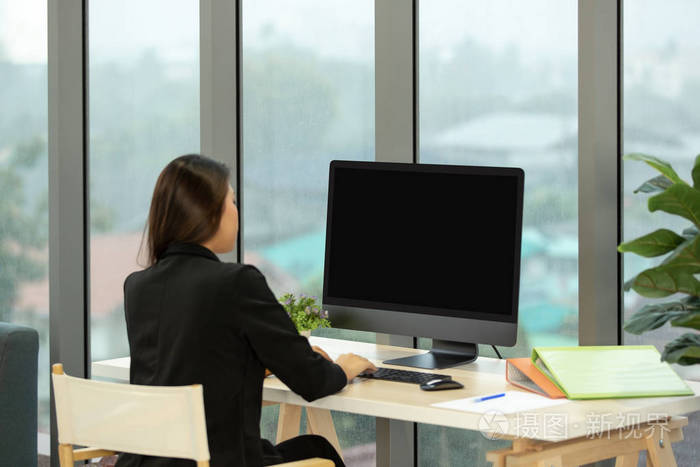 年轻的亚洲女商人坐在电脑黑屏前的现代办公窗口和落下的雨