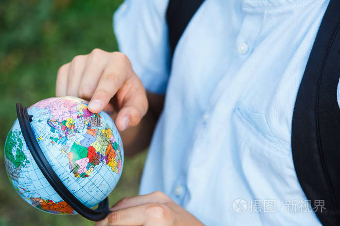 可爱的小男孩穿着蓝色衬衫, 背包和工作簿在他的学校前面握着地球仪。教育, 回到学校概念