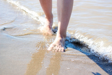 女孩的脚在海滩上。海浪和腿