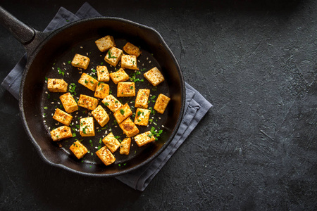 煎豆腐用芝麻和香料放在铸铁锅上, 复制空间。素食素食食谱的健康成分。黑底烤豆腐