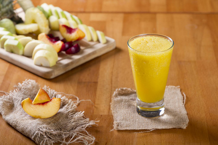美味的健康桃子, 橙色和芒果冰沙在一个鸡尾酒玻璃与新鲜的水果在质朴的木材背景。冰沙是一种由混合生果或蔬菜制成的浓饮料。