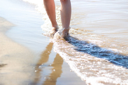 女孩的脚在海滩上。海浪和腿