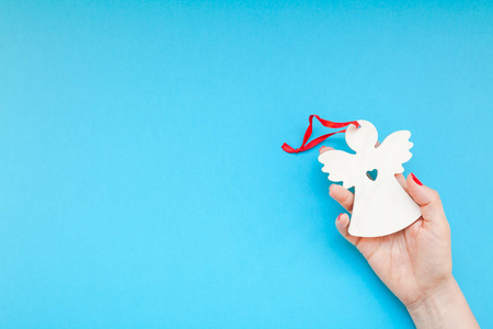 新年或圣诞顶级景观圣诞假期庆祝妇女手红色指甲拿自制木制天使玩具复制空间绿松石蓝色纸张背景最小的风格。模板贺卡