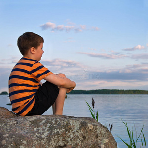 坐在大石头上看海边风景的男孩图片