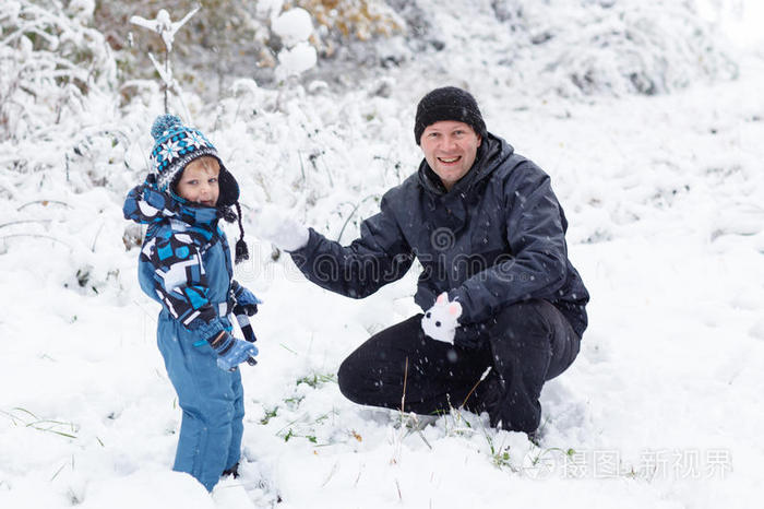 父亲和蹒跚学步的男孩在冬天玩雪