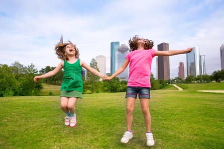两个女孩的朋友在城市的天际线快乐地牵手跳跃