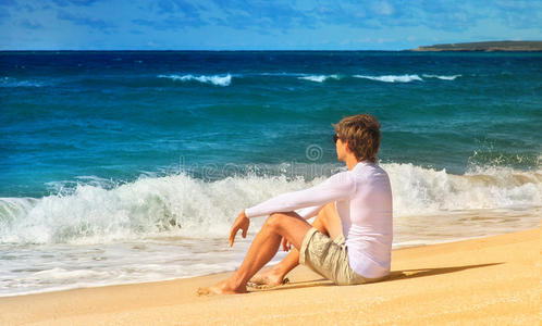 帅哥在沙滩上放松坐在海边沙滩上看海浪夏天的时候