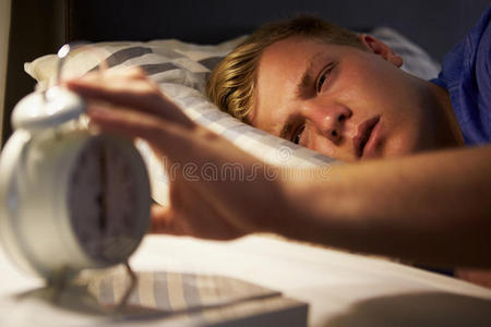 十几岁的男孩在床上醒来，关掉闹钟