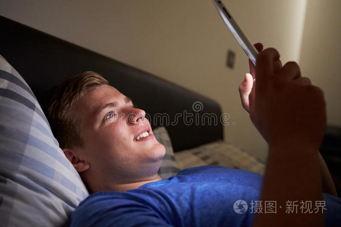 晚上在床上使用数字平板电脑的十几岁男孩