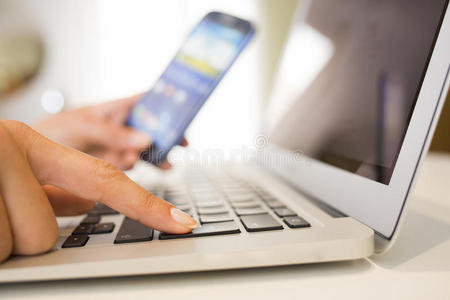 女性手持智能手机和电脑键盘