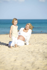 年轻孕妇在沙滩上与女儿玩耍