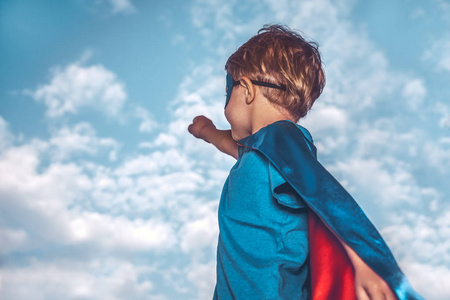小男孩穿着一个超级英雄的服装与举起一只手在天空背景, 准备拯救世界, 孩子玩超人
