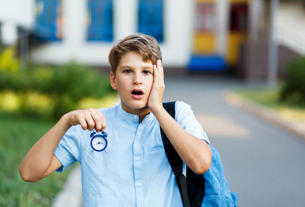 可爱的小男孩穿着蓝色衬衣, 手里拿着钟表。他惊讶的脸。教育, 回到学校概念