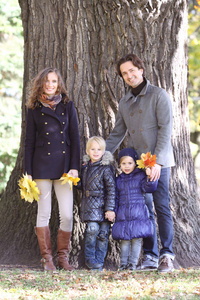 快乐微笑家庭的父母和孩子们在秋季公园站在大树主干附近