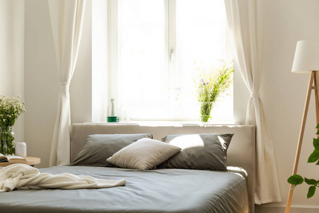 一个舒适的床与石墨床上用品和垫子对一个明亮的窗口在一个绿色的友好卧室内部的一个公寓在树林里。真实照片