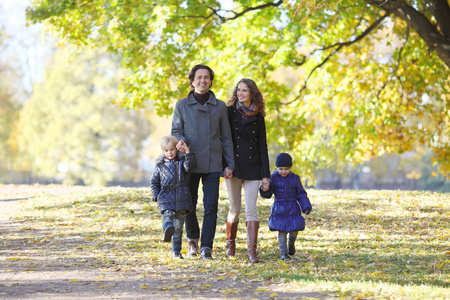幸福的家庭带着两个孩子走在阳光明媚的秋日公园牵着手