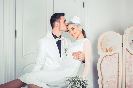 额头上的花时尚男子手持美丽的新娘手和亲吻在额头上站在优雅的内饰