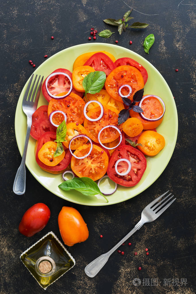 黄色和红色新鲜西红柿沙拉与罗勒和洋葱在一个黑暗的乡村背景.