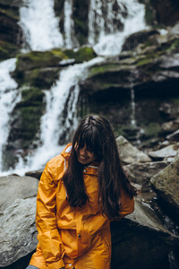 微笑的女人穿着黄色的雨衣, 背景是瀑布。徒步旅行概念