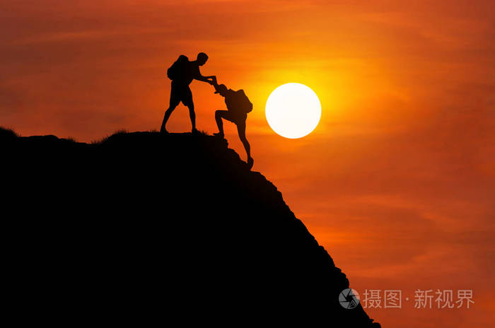 剪影登山手帮助他的朋友一起攀登高峭壁山.团队合作成功理念