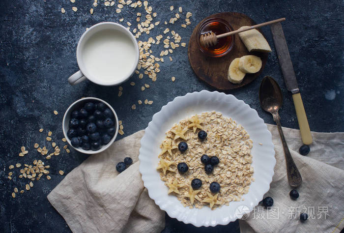 有机燕麦粥与蓝莓, 香蕉, 蜂蜜和牛奶在黑暗的石桌上, 健康的生活方式