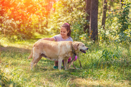 夏天在森林里抚摸拉布拉多猎犬狗的快乐少女的肖像