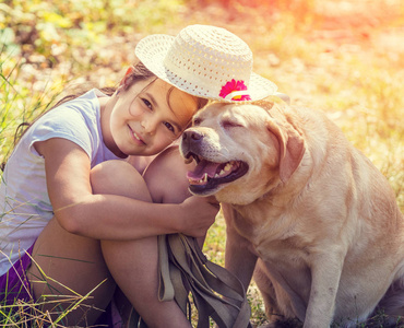 夏天在森林里拥抱狗的快乐女孩的肖像。狗和女孩一起戴着一顶太阳帽