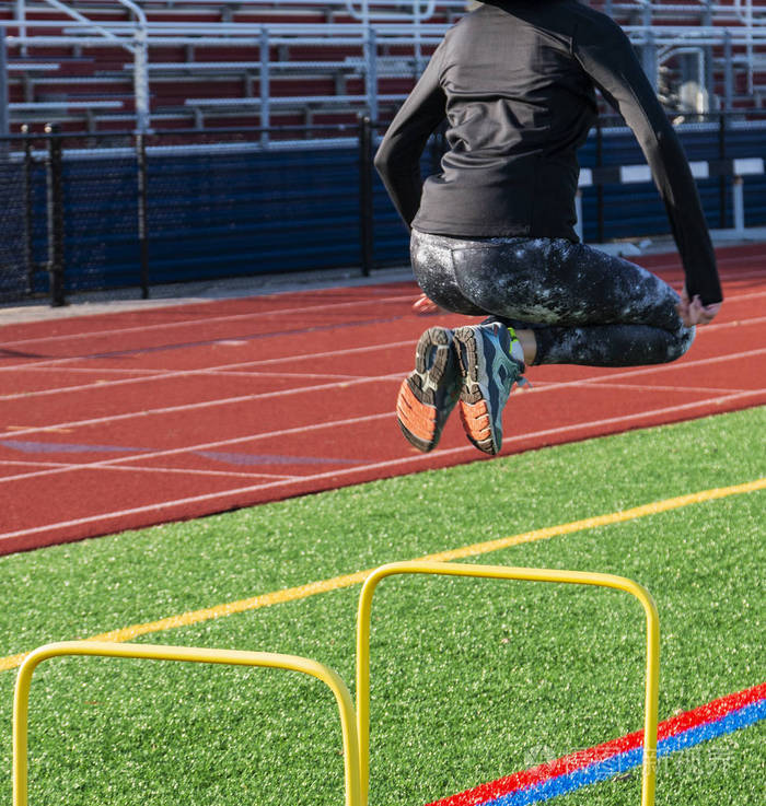 运动员正跳过两英尺黄跨栏, 以 strenctgh, 平衡和协调在一个绿色草皮