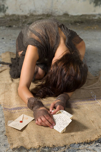 沮丧或害怕躺在肮脏的地板上,一封信在她手中的衣衫褴褛的年轻女子