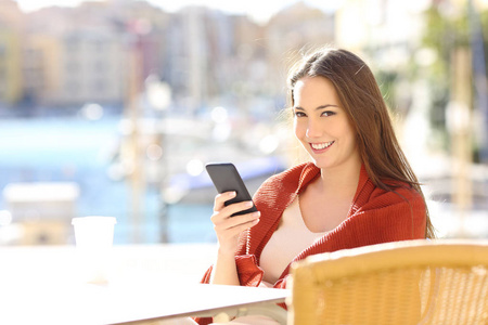 一个快乐的女人拿着一个智能手机在咖啡馆里看着你在海岸镇街
