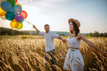 爱夫妇与气球, 休闲在黑麦领域在日落。美丽的妻子和丈夫漫步在夏日的草地上