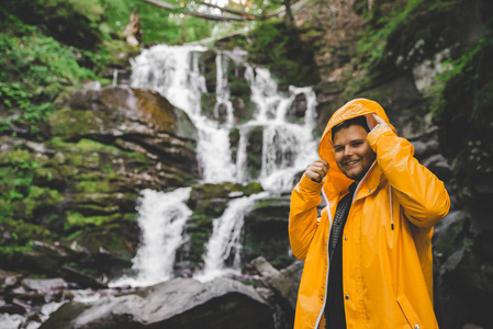 男子站在黄色的雨衣, 看着瀑布。徒步旅行概念