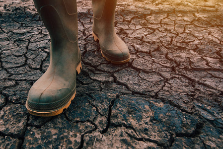 农民穿着橡胶靴行走在干燥的土地上, 全球变暖和气候变化正在影响农